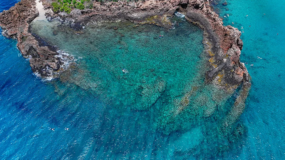 Close-up of the volcanic Black Rock formation at Ka'anapali Beach, Maui, with waves gently crashing around it.
