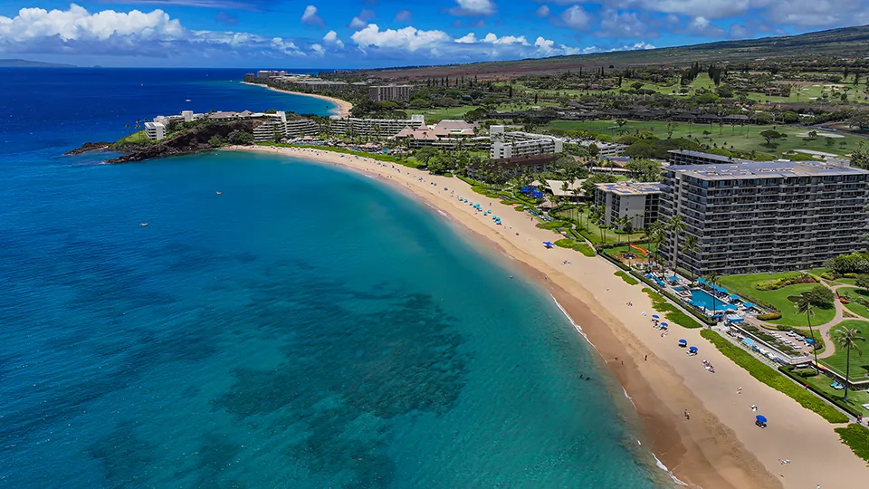 Wide aerial shot of Black Rock Beach and Ka'anapali Beach with visitors swimming and sunbathing along the sandy shoreline.