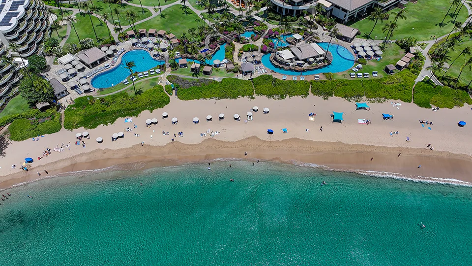 Aerial view of Ka'anapali Beach in Maui showing golden sand, turquoise waters, and beachfront resorts under a bright blue sky.