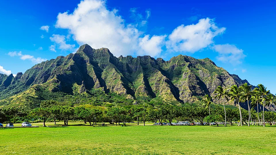 Scenic landscape of Kualoa Ranch on Oahu with lush green pastures and the dramatic Ko'olau Mountain Range in the background.