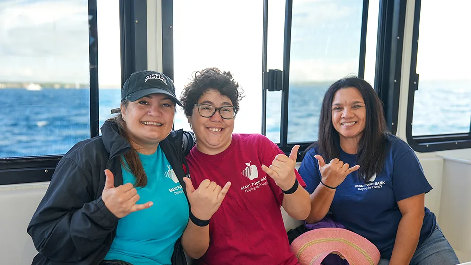 Maui Food Bank volunteers smiling and doing shakas in the cabin of Pride of Maui's 'Elua