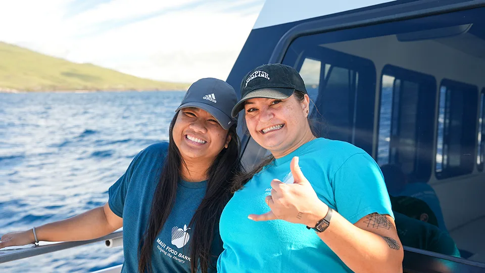 Maui Food Bank volunteers smiling and doing shakas on the deck of Pride of Maui's 'Elua