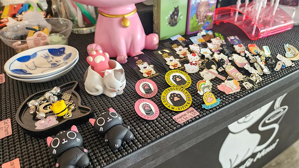 Cat-themed merchandise display at Cat Cafe Maui featuring pins, keychains, and cat ear accessories supporting rescue cat adoptions