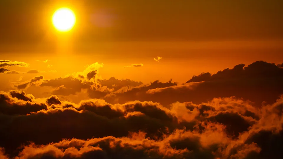 Sunset view above the clouds from Haleakalā Summit in Maui, with warm orange tones and silhouetted cloudscape.