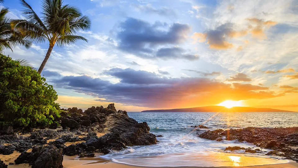 Sunset view at Secret Beach framed by rugged black lava rock and a splash of waves.