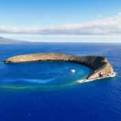 Molokini Crater with Maui in the distance on a calm morning.