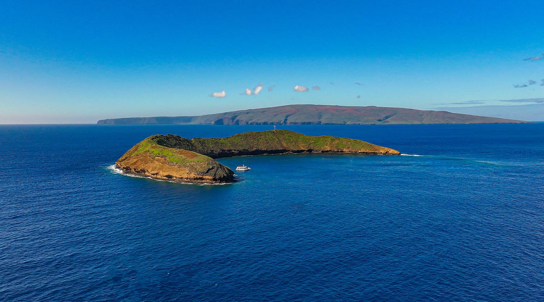 Molokini Crater with Maui in the distance on a calm morning.